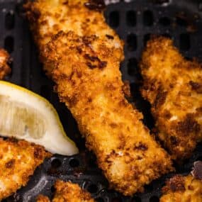 Close up of cooked fish sticks in the air fryer basket.