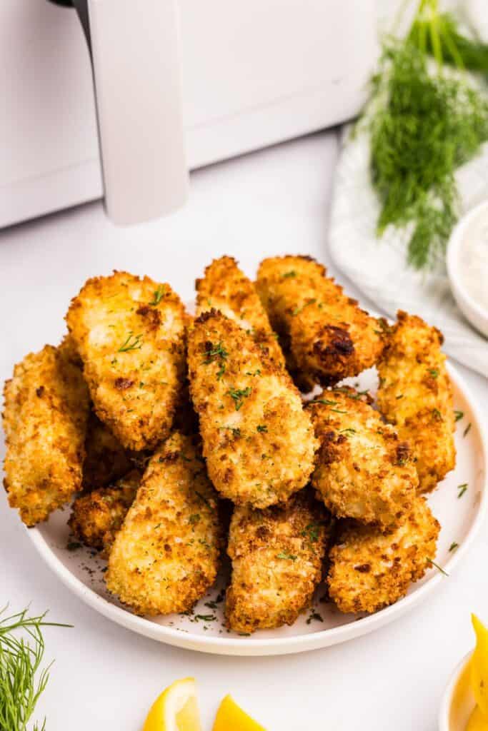 White dinner plate with a large pile of fish sticks stacked on it.