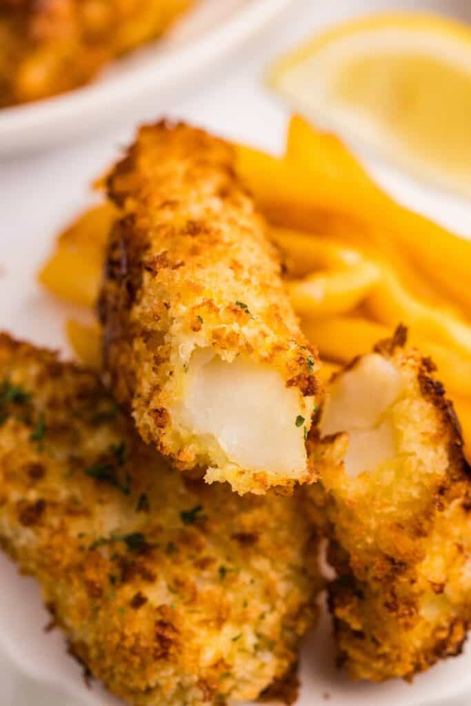 Close up of a pile of fish sticks. One has a bite taken from it.