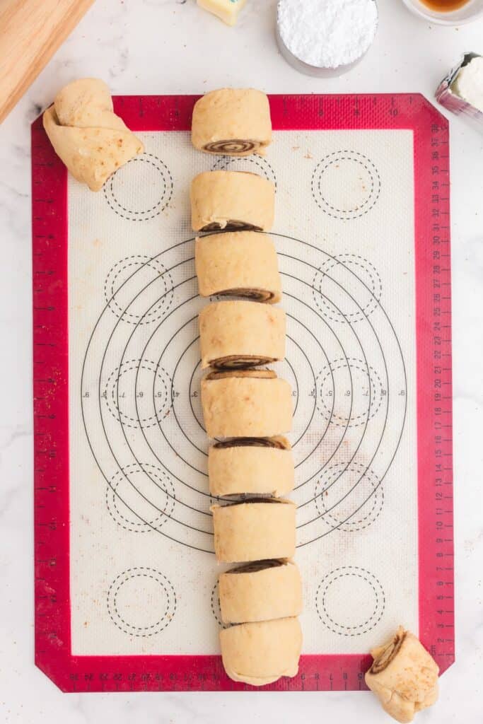 Unbaked cinnamon rolls spiraled and sliced on a silicone baking mat.