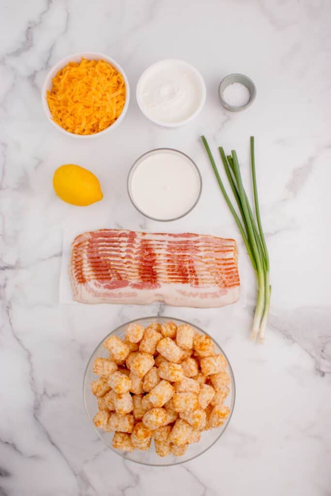 Ingredients for loaded tater tots: Tater tots, cheddar cheese, bacon, sour cream, heavy cream, green onions, lime juice, and salt.