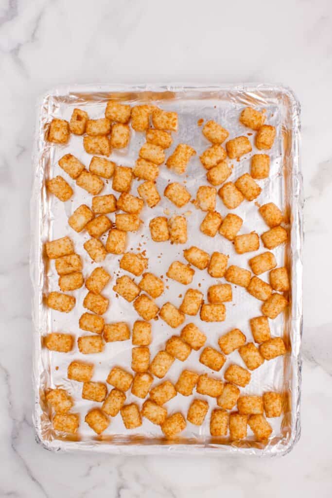 Cooked tater tots on an aluminum covered baking sheet.