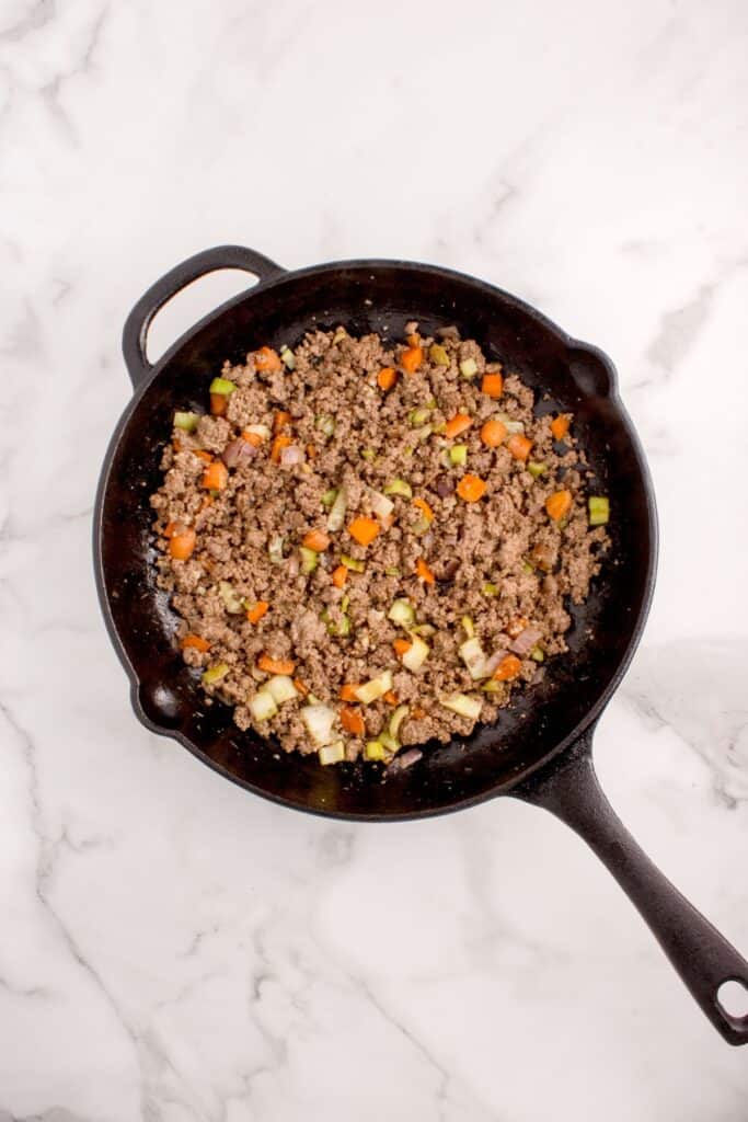 Ground beef, celery, carrots, and onion cooking down in a large skillet.