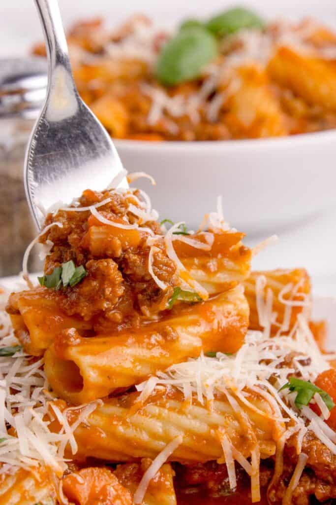 A fork is lifting a bite of rigatoni pasta.