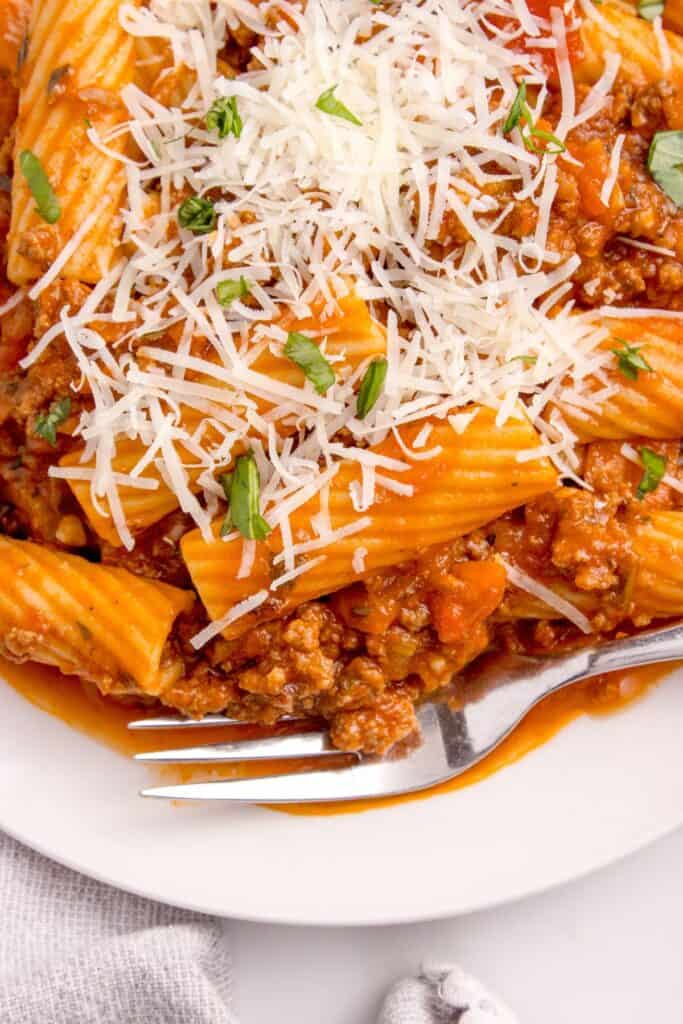 Close up of pasta on a white dinner plate with grated parmesan cheese. A fork sits under the pasta.