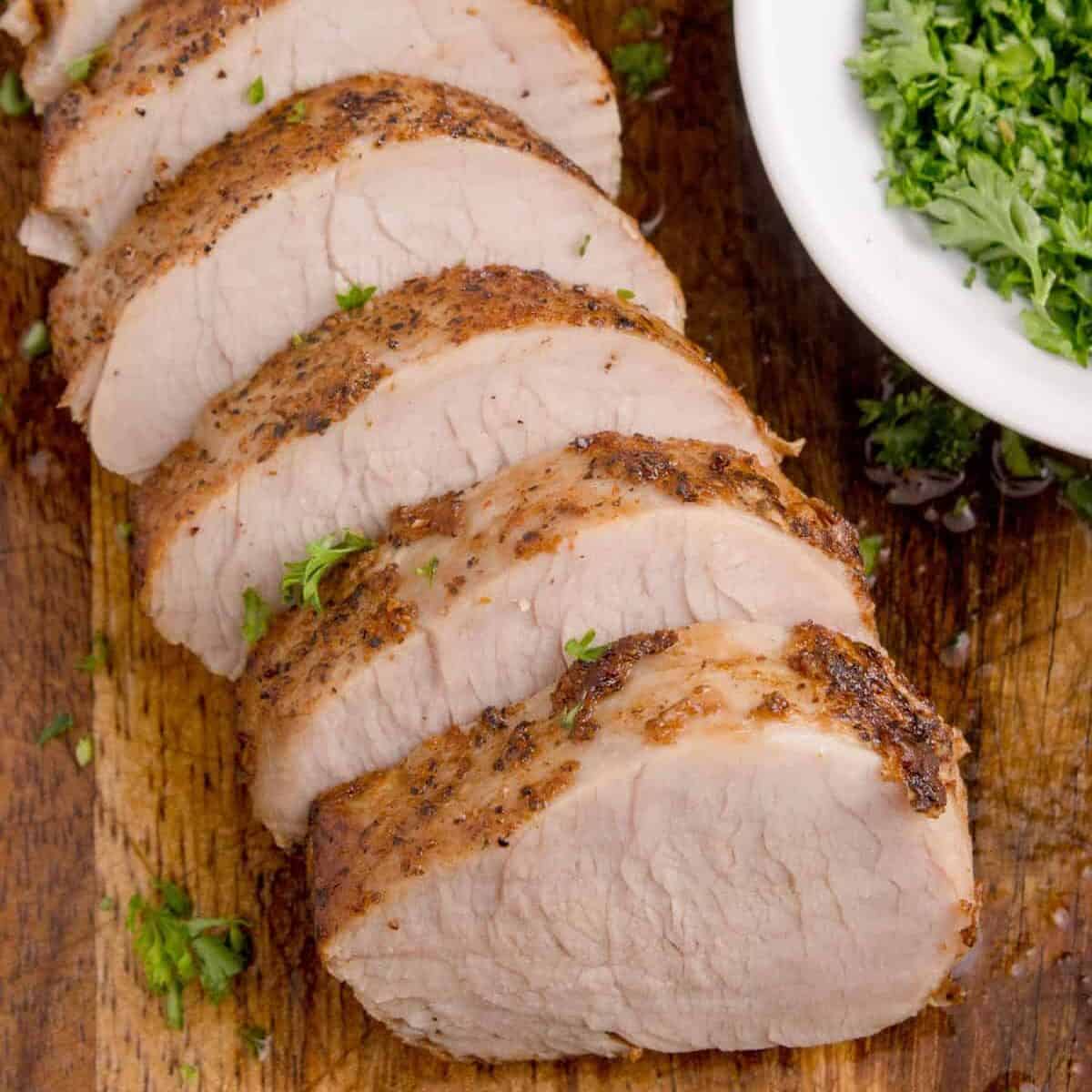 oven baked pork tenderloin sliced on a cutting board.