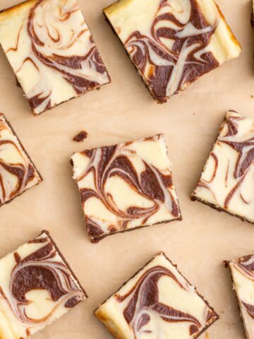 Cheesecake brownies cut and spread out on a sheet of parchment paper.