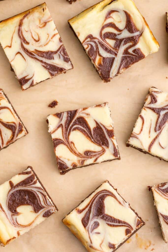 Cheesecake brownies cut and spread out on a sheet of parchment paper.