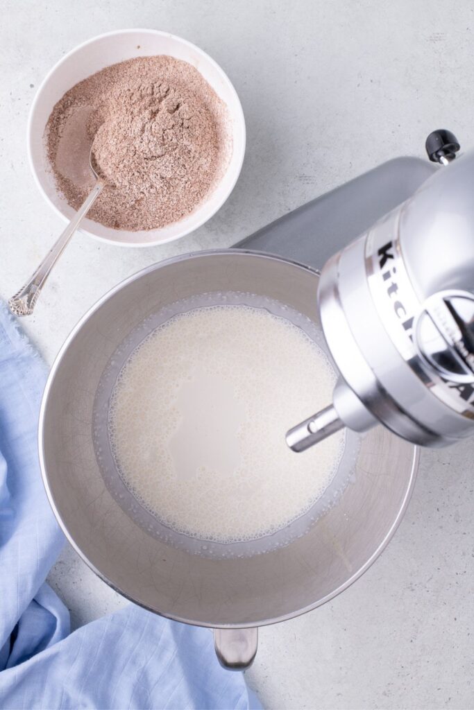 Mixer with cream in mixing bowl. A second bowl is next to it with a mixture of cocoa powder and powdered sugar.