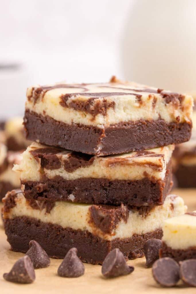 Close up of cream cheese brownies stacked on top of each other with chocolate chips in the front.