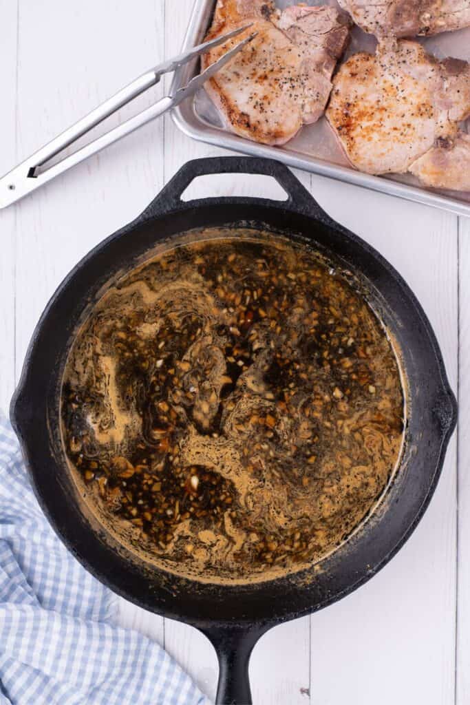 Honey garlic sauce in a cast iron pan. Seared pork chops are prepped on a baking sheet.