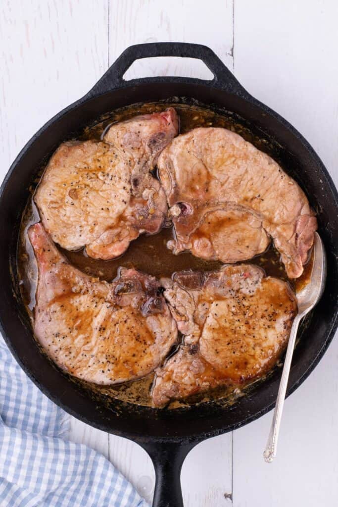 bone in pork chops being pan fried in a cast iron skillet.