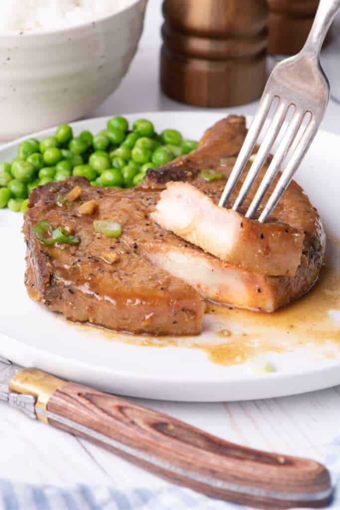 White dinner plate with a pork chop and serving of peas. Pork chop has been sliced into to show interior.