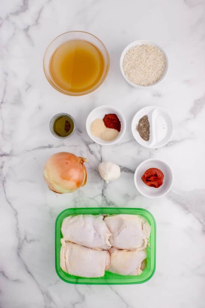 Ingredients for Chicken and rice in a pot: chicken thighs, onion powder, garlic powder, paprika, salt, black pepper, olive oil, yellow onion, garlic, tomato paste, long-grain rice, and chicken stock.