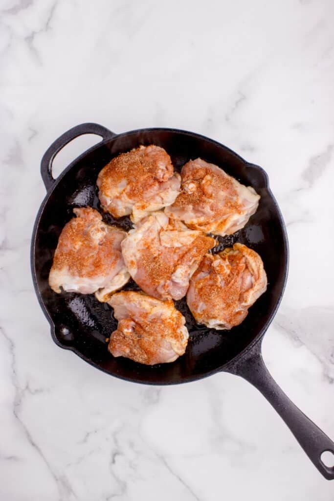 Seasoned chicken being seared in a cast iron pan.