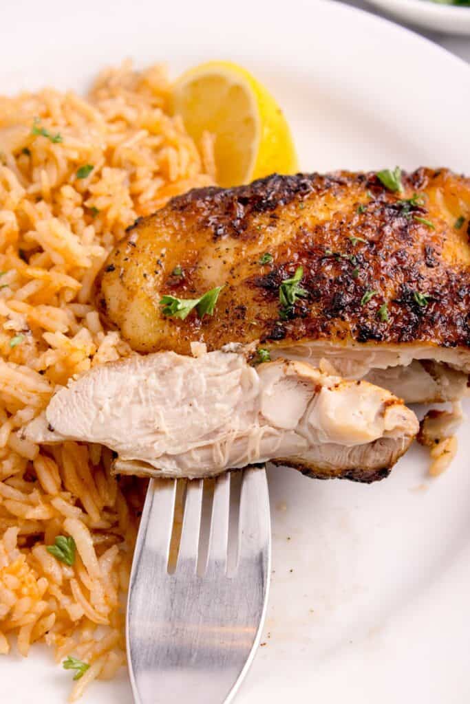 Chicken and rice on white dinner plate. Chicken is sliced and on a fork to show interior.