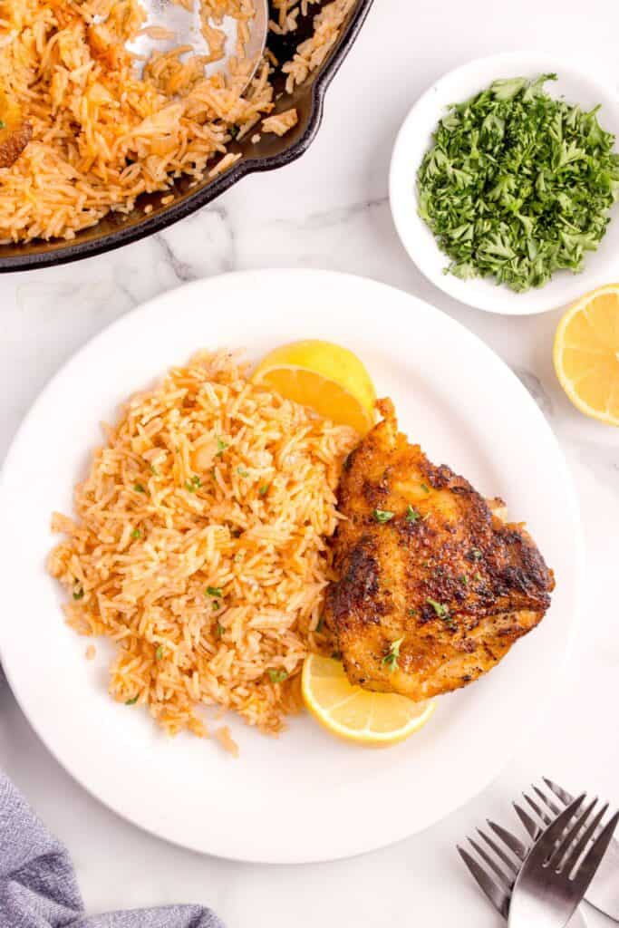 White dinner plate with chicken, rice, and lemon wedges on it.