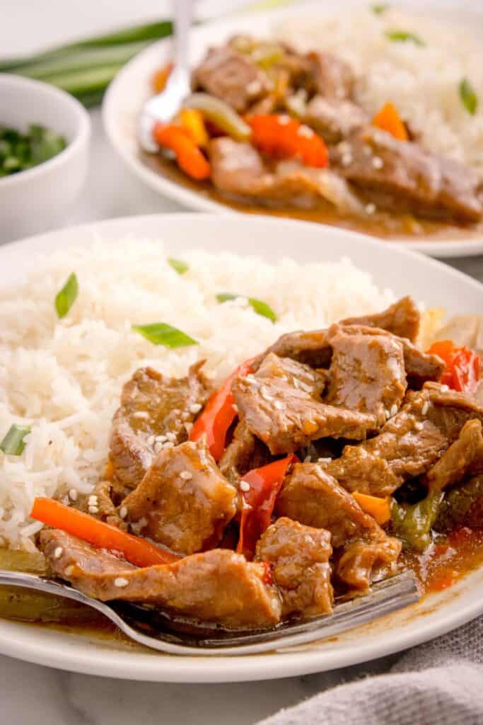 Slow cooker pepper steak served on a white dinner plate with rice.