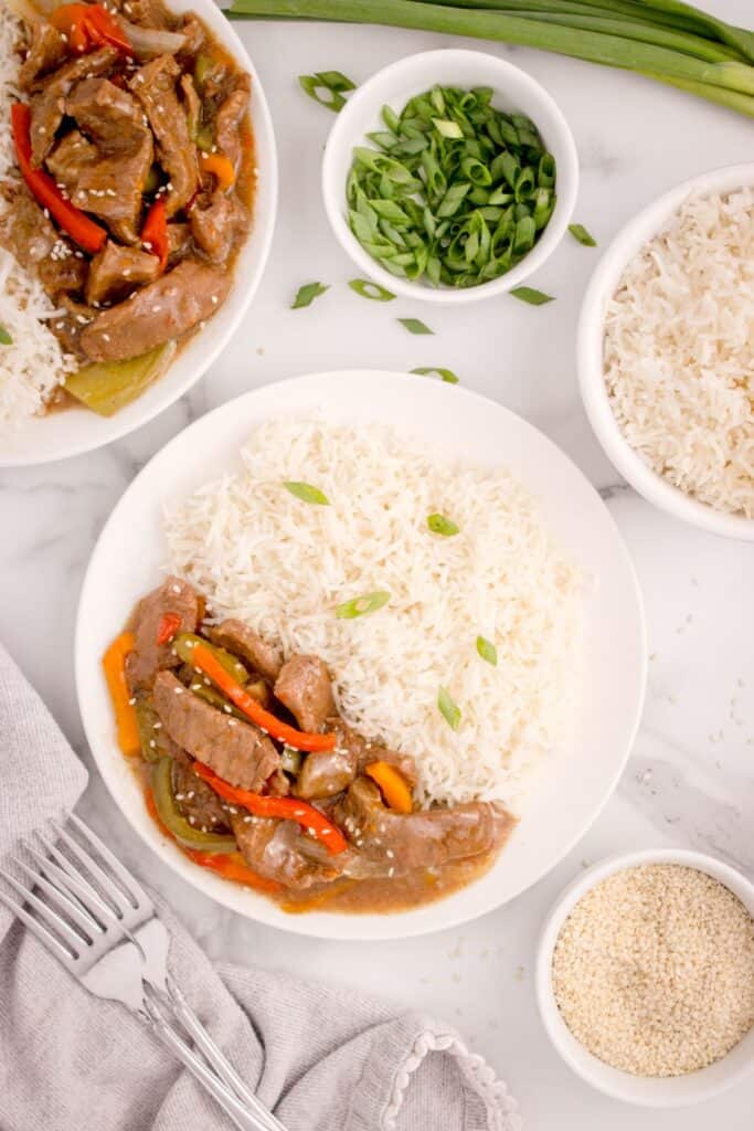 Slow cooker pepper steak served on a white dinner plate with rice.