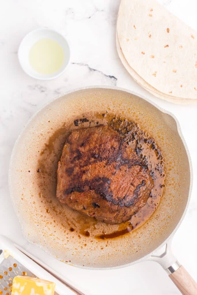 Flank steak cooking in a skillet.