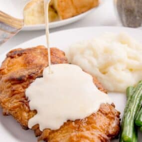 chicken fried chicken on a plate with gravy being poured on it.