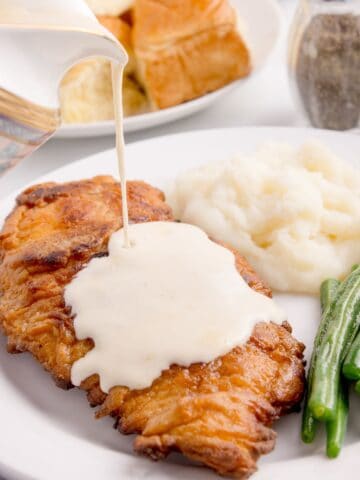 chicken fried chicken on a plate with gravy being poured on it.