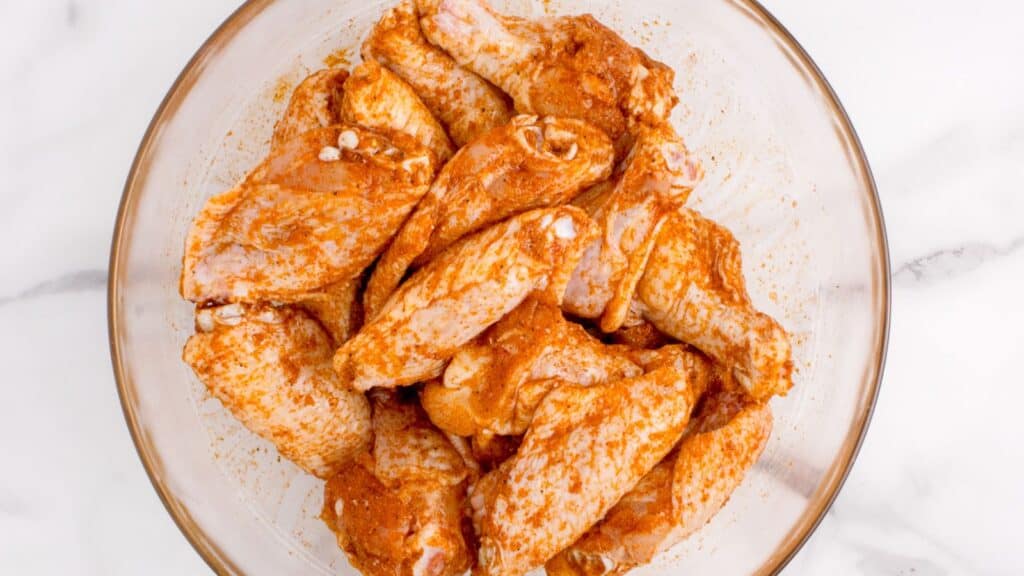 raw chicken wings in a bowl tossed in seasonings