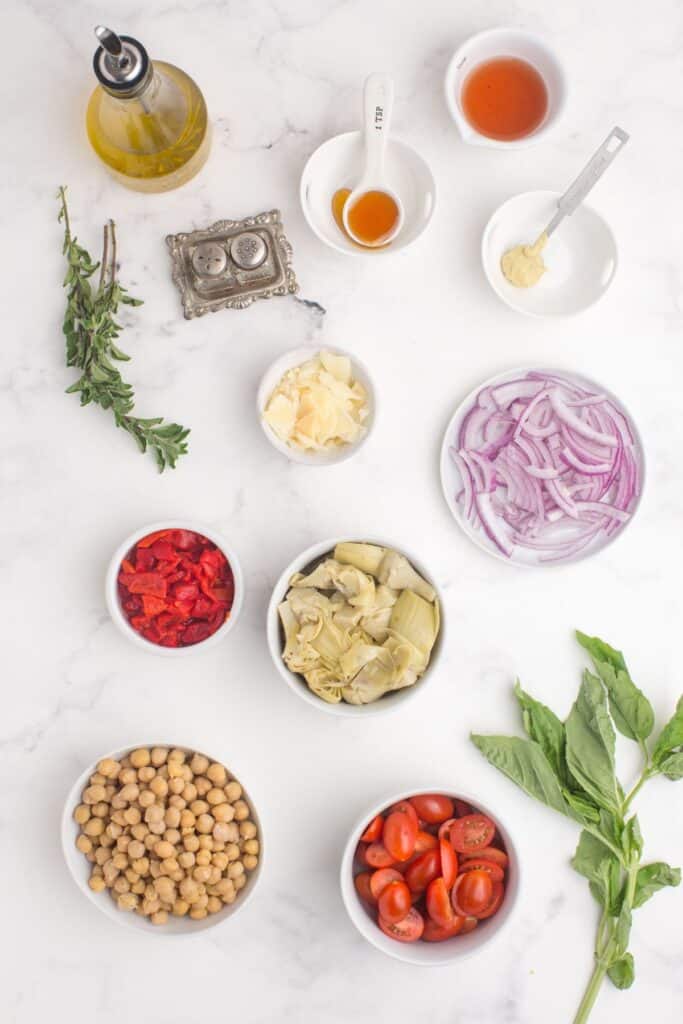 Ingredients for artichoke salad: marinated artichokes, chickpeas, cherry tomatoes, red onion, fresh basil, shaved parmesan, olive oil, red wine vinegar, Dijon mustard, honey, garlic powder, fresh oregano, and basil.