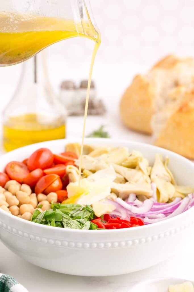 Components of artichoke salad in a serving bowl with the homemade dressing poured over the top.