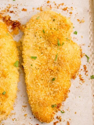 Baked parmesan crusted chicken on a parchment lined baking sheet.