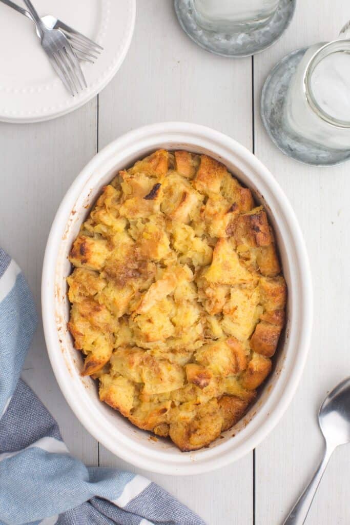 Baked pineapple stuffing surrounded by dinner plates, forks, glasses of water, and a serving spoon.