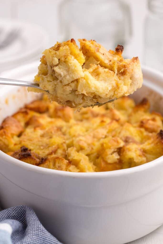 A bite of pineapple stuffing lifted above a baking dish full of stuffing.