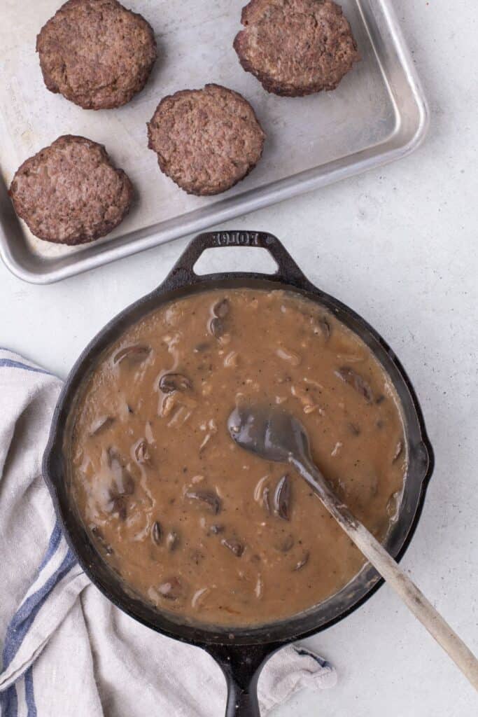 Hamburger steak gravy in a cast iron pan. Hamburger patties on the side on a baking pan.