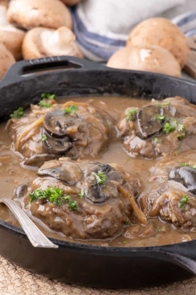 Cast iron pan with cooked hamburger steak in a gravy.