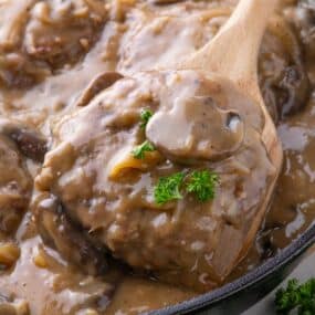 Cast iron pan with cooked hamburger steak in a gravy.