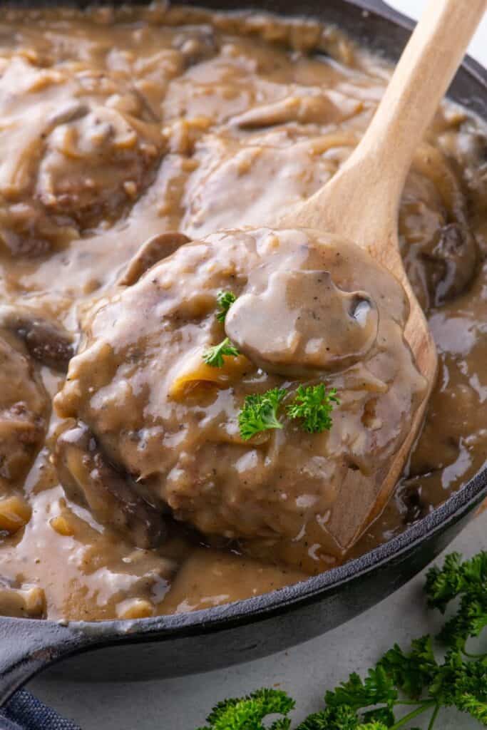 Cast iron pan with cooked hamburger steak in a gravy.